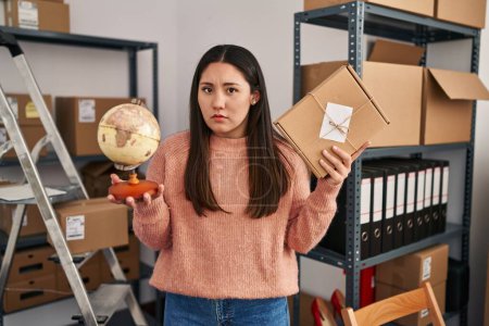 Photo for Young latin woman working at small business ecommerce doing world shipping clueless and confused expression. doubt concept. - Royalty Free Image