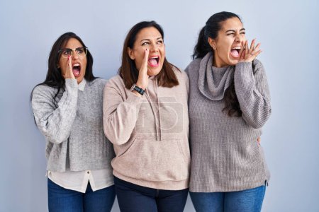 Photo for Mother and two daughters standing over blue background shouting and screaming loud to side with hand on mouth. communication concept. - Royalty Free Image