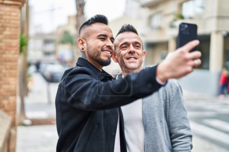 Foto de Dos hombres pareja sonriendo confiado hacer selfie por teléfono inteligente en la calle - Imagen libre de derechos