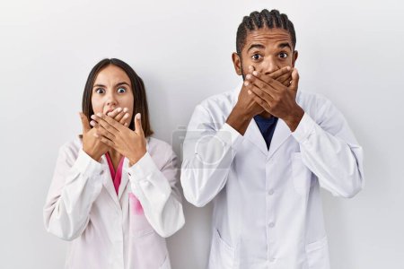 Téléchargez les photos : Jeunes médecins hispaniques debout sur fond blanc choqué couvrant la bouche avec les mains pour erreur. concept secret. - en image libre de droit