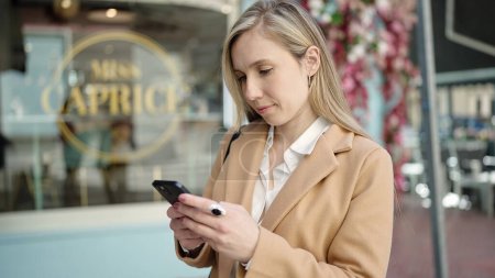 Téléchargez les photos : Jeune femme blonde utilisant smartphone debout sur la terrasse du café - en image libre de droit