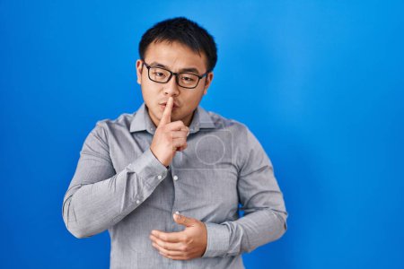 Photo for Young chinese man standing over blue background asking to be quiet with finger on lips. silence and secret concept. - Royalty Free Image