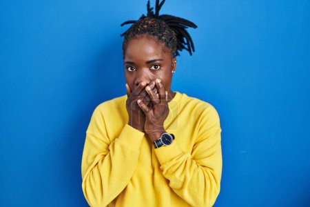 Photo for Beautiful black woman standing over blue background shocked covering mouth with hands for mistake. secret concept. - Royalty Free Image