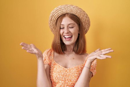 Téléchargez les photos : Jeune femme rousse debout sur fond jaune portant un chapeau d'été célébrant fou et fou de succès avec les bras levés et les yeux fermés hurlant excités. concept gagnant - en image libre de droit