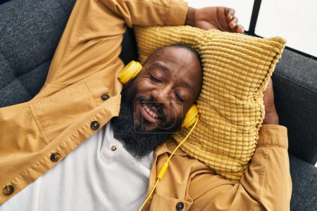 Photo for Young african american man listening to music lying on sofa at home - Royalty Free Image