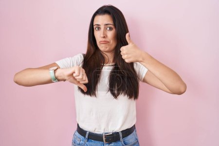 Photo for Young brunette woman standing over pink background doing thumbs up and down, disagreement and agreement expression. crazy conflict - Royalty Free Image