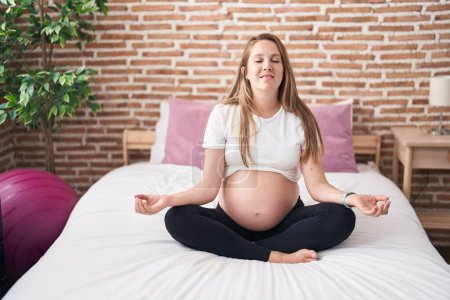 Téléchargez les photos : Young pregnant woman doing yoga exercise sitting on bed at bedroom - en image libre de droit