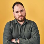 Plus size hispanic man with beard standing over yellow background skeptic and nervous, disapproving expression on face with crossed arms. negative person.