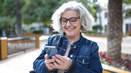 Photo for Middle age woman with grey hair using smartphone at park - Royalty Free Image