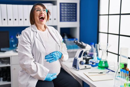 Photo for Pregnant woman working at scientist laboratory angry and mad screaming frustrated and furious, shouting with anger. rage and aggressive concept. - Royalty Free Image