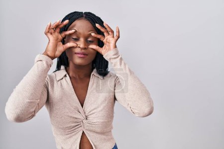 Téléchargez les photos : Femme africaine avec des tresses debout sur fond blanc essayant d'ouvrir les yeux avec les doigts, somnolente et fatiguée pour la fatigue matinale - en image libre de droit