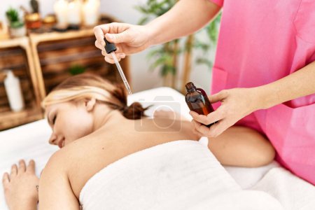 Photo for Young caucasian woman lying on table having back massage using oil at beauty salon - Royalty Free Image