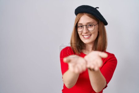 Photo for Young redhead woman standing wearing glasses and beret smiling with hands palms together receiving or giving gesture. hold and protection - Royalty Free Image