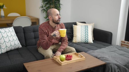 Photo for Young bald man having breakfast sitting on sofa at home - Royalty Free Image