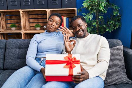 Téléchargez les photos : Jeune couple afro-américain tenant présent faire ok signe avec les doigts, sourire geste amical excellent symbole - en image libre de droit