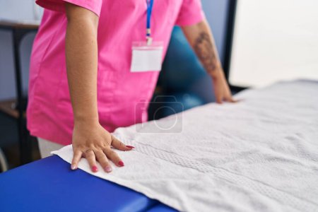 Téléchargez les photos : Jeune belle hispanique femme pysiothérapeute mettre serviette sur table de massage à la clinique de réadaptation - en image libre de droit