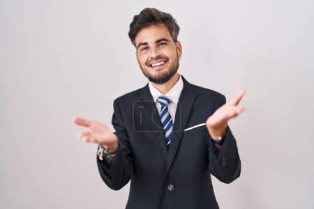 Photo for Young hispanic man with tattoos wearing business suit and tie smiling cheerful offering hands giving assistance and acceptance. - Royalty Free Image