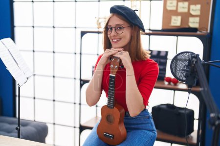 Téléchargez les photos : Jeune rousse femme musicien souriant confiant tenant ukulele au studio de musique - en image libre de droit