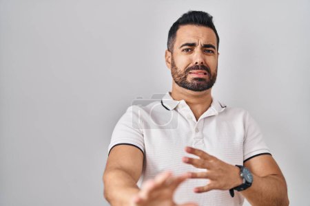 Téléchargez les photos : Young hispanic man with beard wearing casual clothes over white background disgusted expression, displeased and fearful doing disgust face because aversion reaction. - en image libre de droit