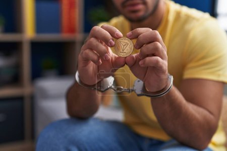 Photo for Young hispanic man criminal holding tron crypto currency wearing handcuffs at home - Royalty Free Image