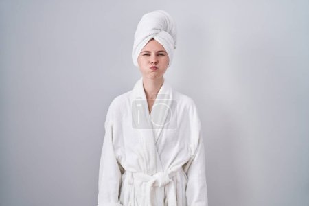 Téléchargez les photos : Blonde caucasian woman wearing bathrobe puffing cheeks with funny face. mouth inflated with air, crazy expression. - en image libre de droit