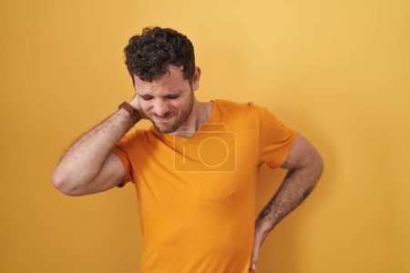 Téléchargez les photos : Young hispanic man standing over yellow background suffering of neck ache injury, touching neck with hand, muscular pain - en image libre de droit