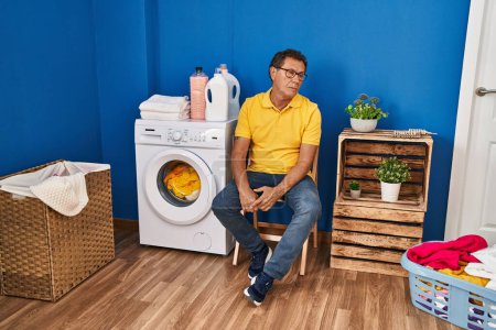 Téléchargez les photos : Middle age man sitting on chair waiting for washing machine at laundry room - en image libre de droit