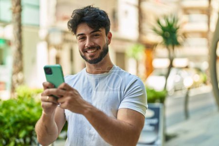 Photo pour Jeune homme hispanique souriant confiant en utilisant un smartphone dans la rue - image libre de droit
