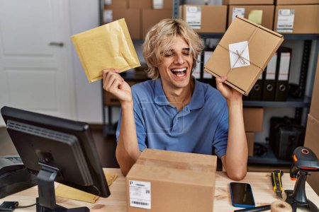 Foto de Young man working at small business ecommerce holding packages smiling and laughing hard out loud because funny crazy joke. - Imagen libre de derechos