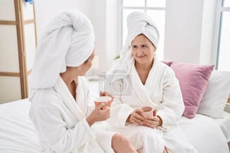 Photo for Mother and daughter wearing bathrobe drinking coffee at bedroom - Royalty Free Image