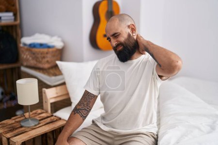 Foto de Young bald man suffering for neck injury sitting on bed at bedroom - Imagen libre de derechos