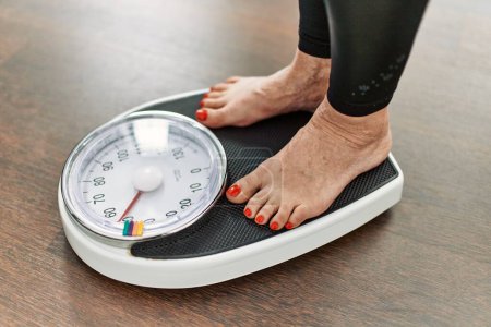 Photo for Middle age grey-haired woman using weighing machine at home - Royalty Free Image