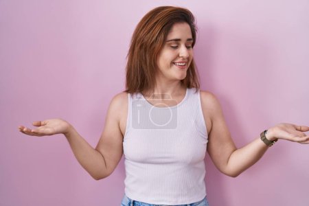 Téléchargez les photos : Femme brune debout sur fond rose souriant montrant les paumes ouvertes des deux mains, présentant et comparant la publicité et l'équilibre - en image libre de droit