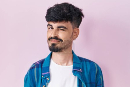 Photo for Young hispanic man with beard standing over pink background winking looking at the camera with sexy expression, cheerful and happy face. - Royalty Free Image