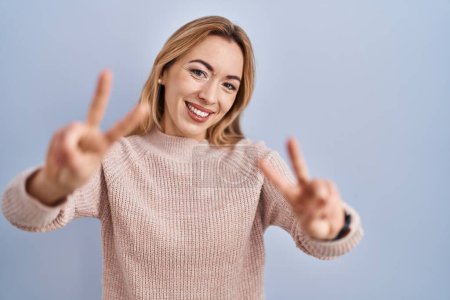 Téléchargez les photos : Femme hispanique debout sur fond bleu souriant avec la langue montrant les doigts des deux mains faisant signe de victoire. numéro deux. - en image libre de droit