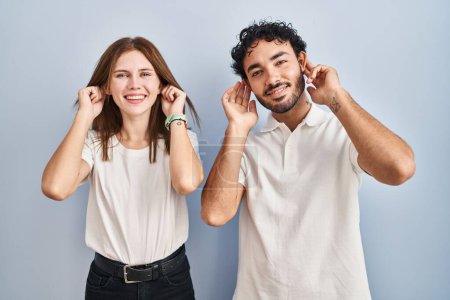 Photo for Young couple wearing casual clothes standing together smiling pulling ears with fingers, funny gesture. audition problem - Royalty Free Image