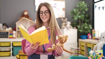 Téléchargez les photos : Young blonde woman preschool teacher reading story book at kindergarten - en image libre de droit