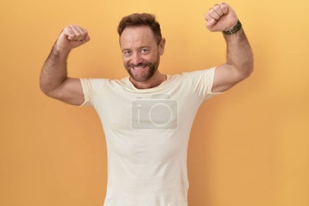 Téléchargez les photos : Homme d'âge moyen avec barbe debout sur fond jaune montrant les muscles des bras souriant fier. concept de fitness. - en image libre de droit