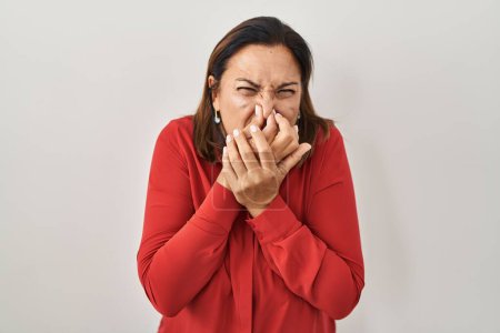 Photo for Hispanic mature woman standing over white background smelling something stinky and disgusting, intolerable smell, holding breath with fingers on nose. bad smell - Royalty Free Image