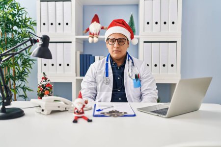 Photo for Hispanic young doctor man at the clinic on christmas with serious expression on face. simple and natural looking at the camera. - Royalty Free Image