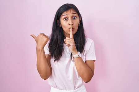 Téléchargez les photos : Young hispanic woman standing over pink background asking to be quiet with finger on lips pointing with hand to the side. silence and secret concept. - en image libre de droit