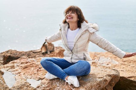 Téléchargez les photos : Middle age woman smiling confident sitting with arms open at seaside - en image libre de droit