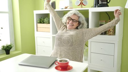Photo for Middle age woman with grey hair using laptop stretching arms at home - Royalty Free Image