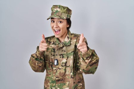 Foto de Young south asian woman wearing camouflage army uniform pointing fingers to camera with happy and funny face. good energy and vibes. - Imagen libre de derechos