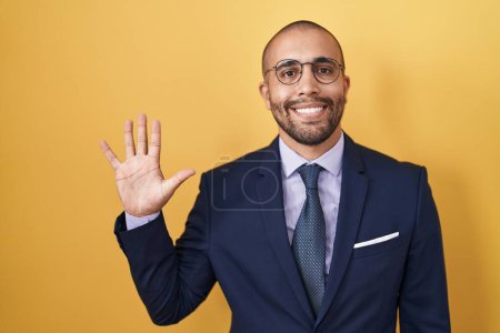 Téléchargez les photos : Homme hispanique avec barbe portant costume et cravate montrant et pointant vers le haut avec les doigts numéro cinq tout en souriant confiant et heureux. - en image libre de droit