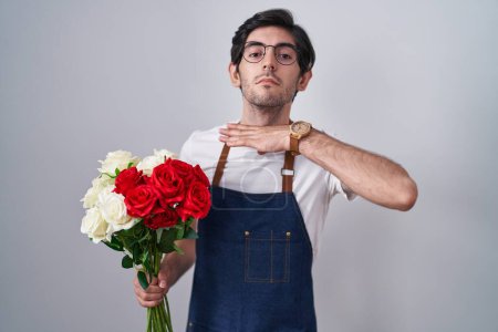 Photo for Young hispanic man holding bouquet of white and red roses cutting throat with hand as knife, threaten aggression with furious violence - Royalty Free Image