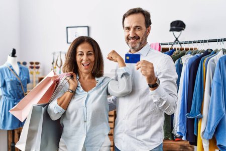 Photo for Hispanic middle age couple holding shopping bags and credit card strong person showing arm muscle, confident and proud of power - Royalty Free Image