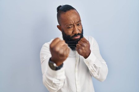 Photo for African american man standing over blue background ready to fight with fist defense gesture, angry and upset face, afraid of problem - Royalty Free Image