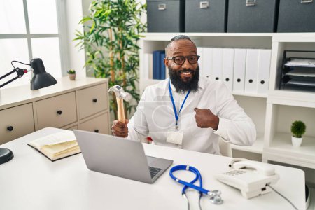 Téléchargez les photos : African american man working at medical clinic holding hammer pointing finger to one self smiling happy and proud - en image libre de droit