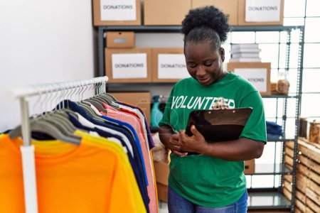Téléchargez les photos : Jeune femme afro-américaine portant un uniforme bénévole tenant un presse-papiers travaillant au centre de charité - en image libre de droit